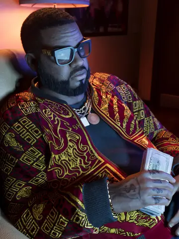 Boobie Ike seated in a leather chair holding cash